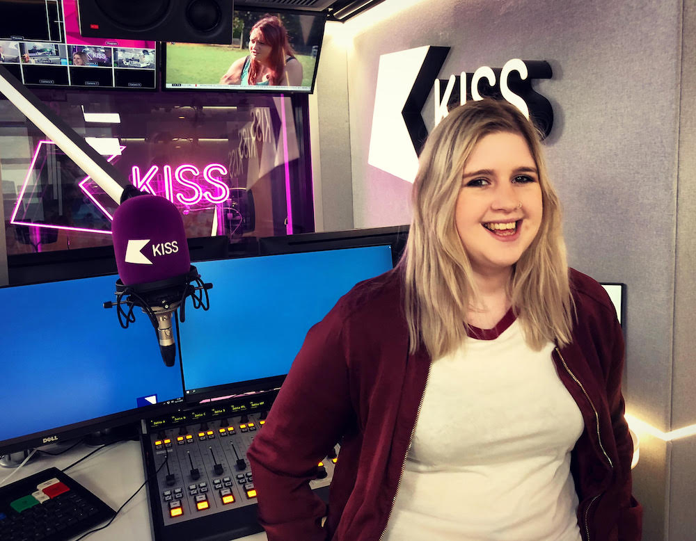 Hannah Austin standing in front of a sound desk and purple microphone in the Kiss studios