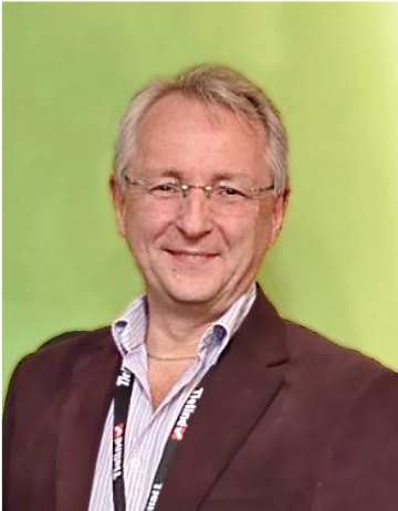 Quentin Howard - white man with grey hair and glasses standing in front of an apple green background and wearing a brown suit with light shirt and lanyard.