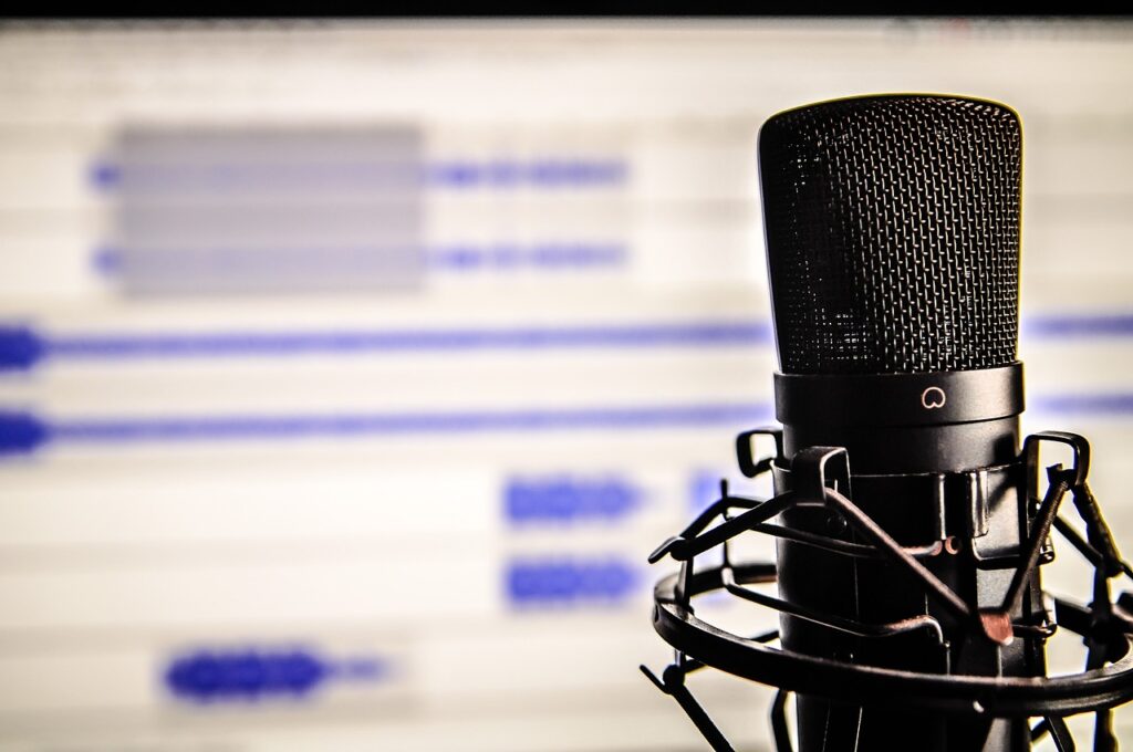 Close up of a black microphone with a blurred audio editing session on screen in the background.