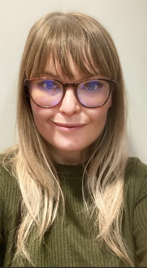 Vanessa Tarrier - white woman with long blond hair past her shoulders and large tortoiseshell glasses. She's wearing a light olive green top.