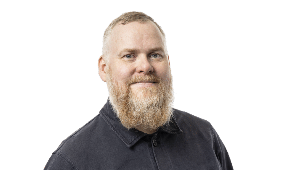 Jørgen - a middle-aged white man with blue eyes, a dark denim shirt, short hair and long ginger-grey beard. He looks like a Viking and is smiling at us. 